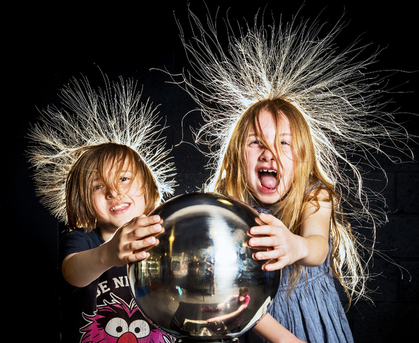 A boy and a girl touch a ball which causes their hair to stand on end