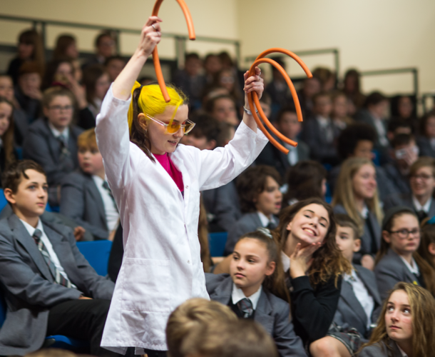 An Inspirer in a lab coat engages an audience of school pupils in a science demonstration