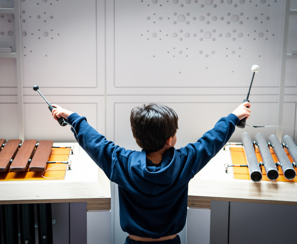 Interactive science exhibition photo showing a young boy holding his hands in the air above the glockenspiel