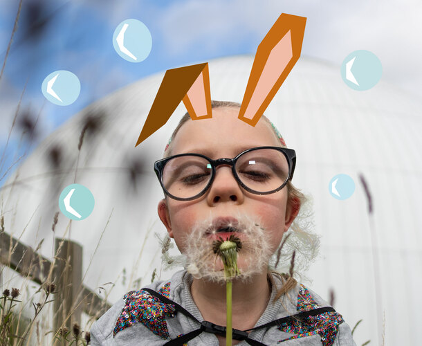 A little girl with illustrated rabbit ears blows a dandelion