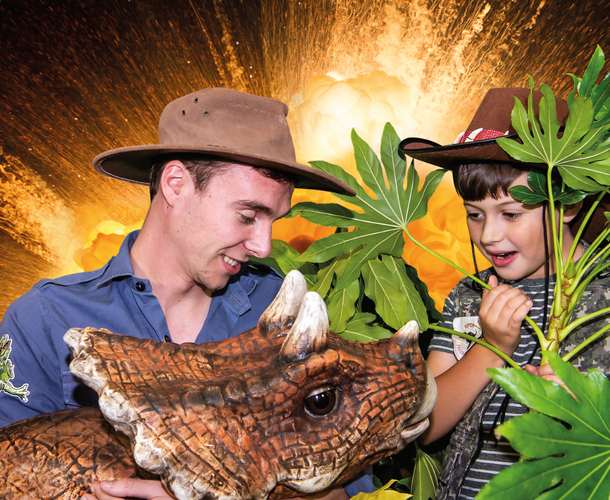 Christmas promotional photo showing a young boy looking excitedly at a dinosaur being held by a dino ranger