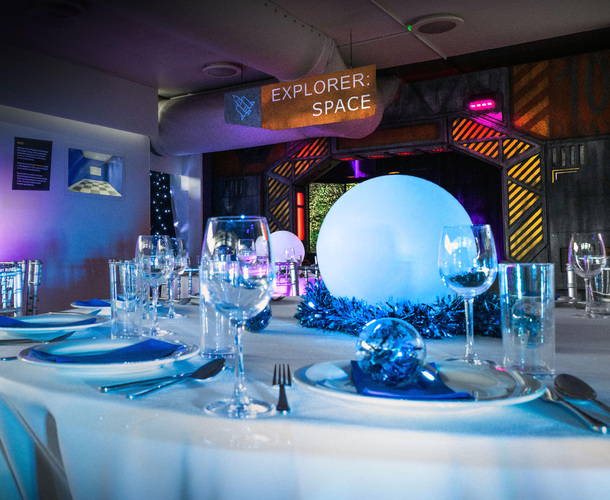 A dinner table with white tablecloth set up for Christmas dinner with space items in the background