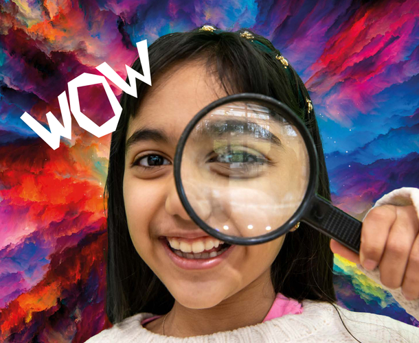 A girl hold a magnifying glass over her eye and smiles