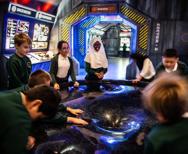 Interactive science exhibition photo showing a group of school children in a circle around a space-related exhibit as part of their school trip