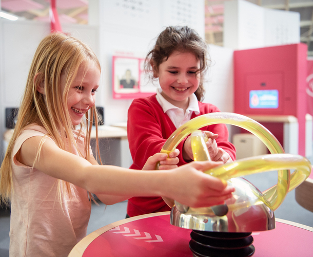 Interactive science exhibition photo showing two girls smiling while interacting with an exhibit