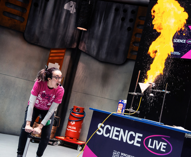Live science demo area photo showing a presenter looking in awe while pushing down on a pump to set fire to corn flour