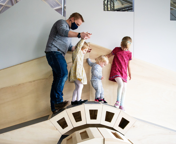 Interactive science exhibition photo showing a dad helping three children walk across a small bridge they have constructed