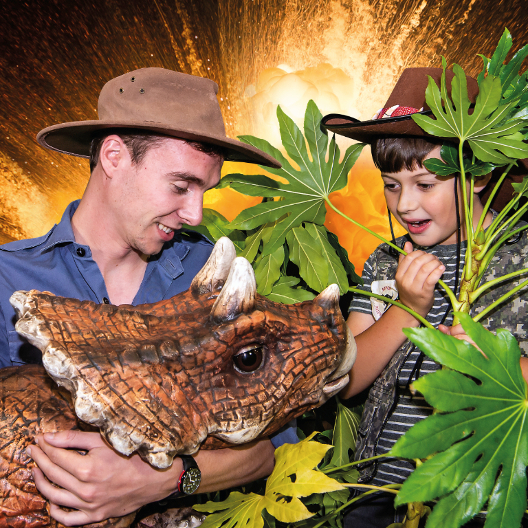 Christmas promotional photo showing a young boy looking excitedly at a dinosaur being held by a dino ranger