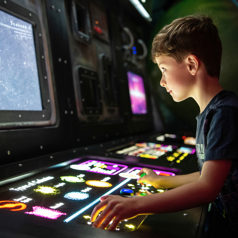A little boy plays with a space exhibit whilst looking at a screen