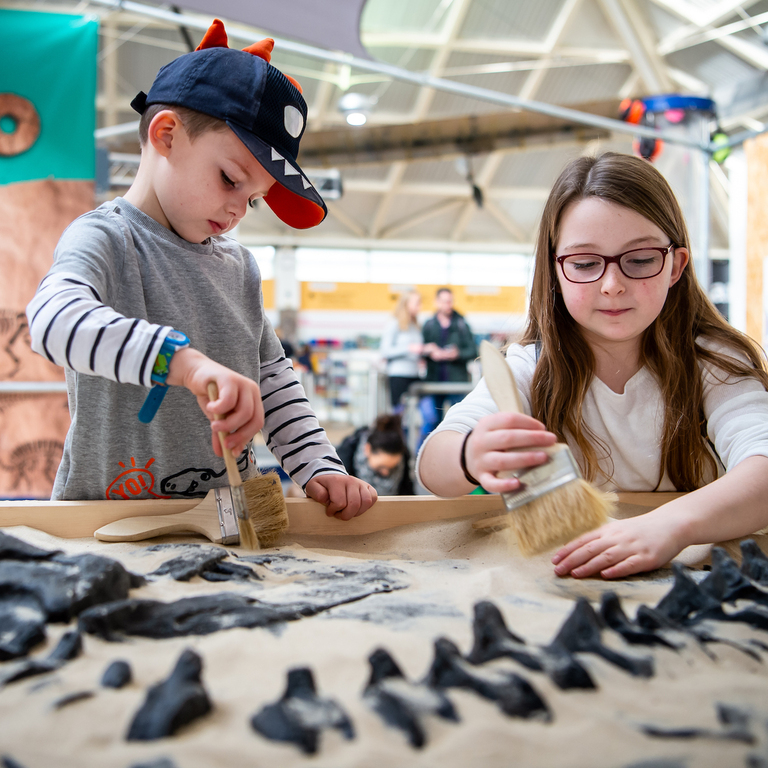 Two young children uncovering hidden bones in the dino dig by brushing the sand away