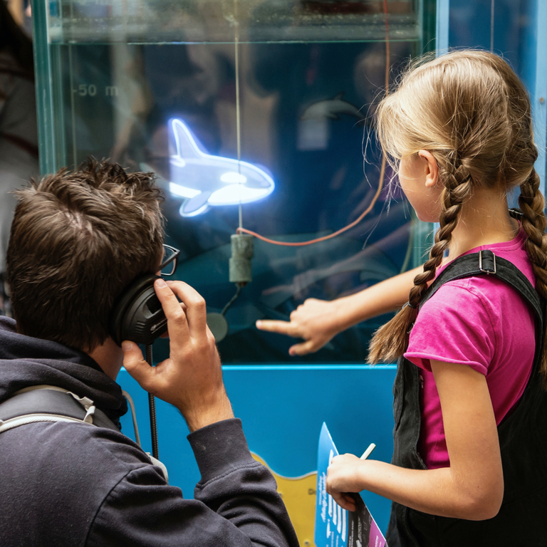 Exhibition photo showing a dad and his daughter listening to a whale sound exhibit