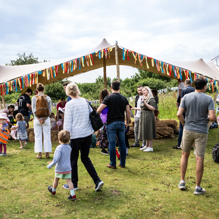 Families gather around a bell tent in a sunny outdoor landscape