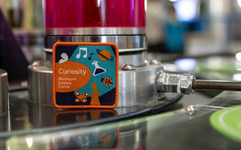 An orange and blue Curiosity Badge