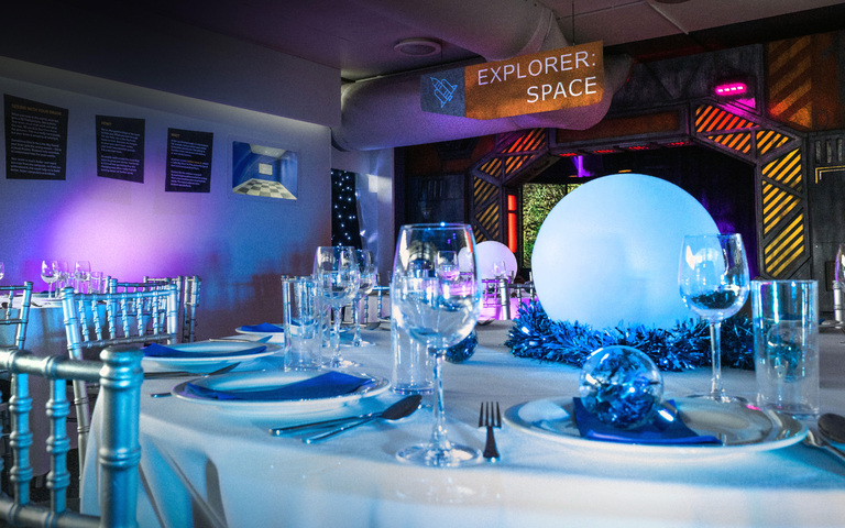 A dinner table with white tablecloth set up for Christmas dinner with space items in the background