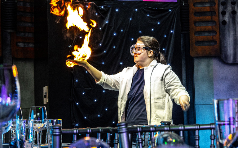 A scientist with her hand on fire behind a festive dinner table