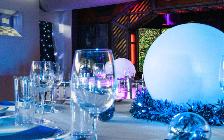 A dinner table with white tablecloth set up for Christmas dinner with space items in the background
