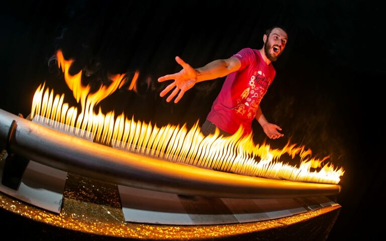 A man waves his hands dramatically over a series of flames coming out of a tube