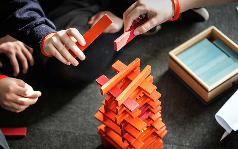 Children's hands placing pieces of wood in order to form a stacked tower