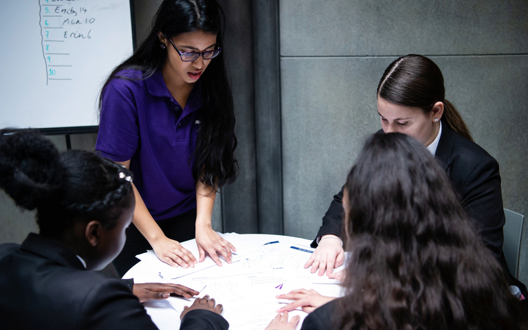 Four female students around a round table studying worksheets together