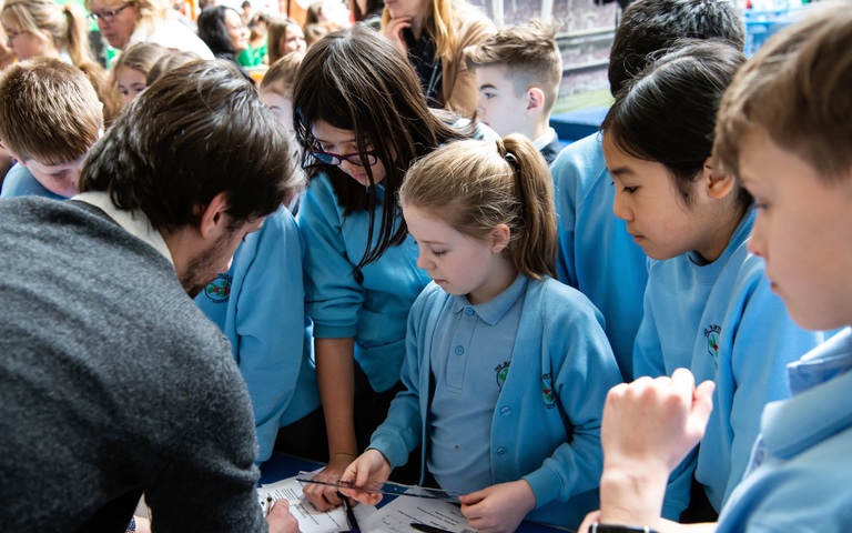 A group of children in uniform looking at what a teacher is writing down