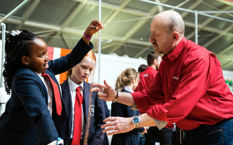 A girl in school uniform and a STEM Ambassador stretching out a metal spring