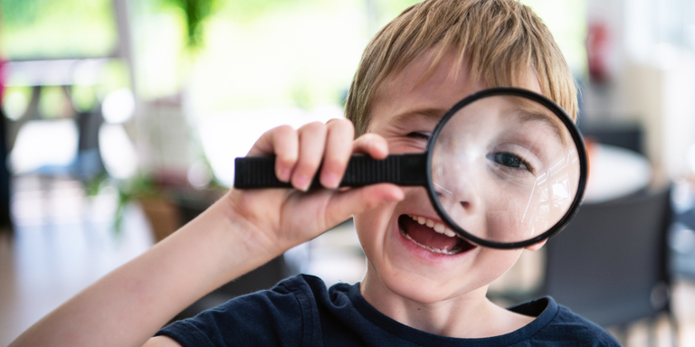 A young boy laughs as he peers through a magnifying glass