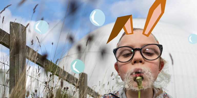 A little girl with illustrated rabbit ears blows a dandelion
