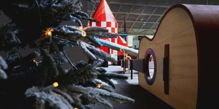 A snowy Christmas tree with a giant guitar and red and white rocket behind it