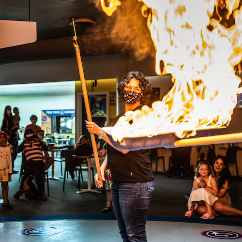 A lady assisting the presenter with a demonstration involving fire