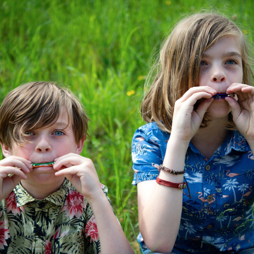 Two boys sitting outside testing the harmonicas they have made