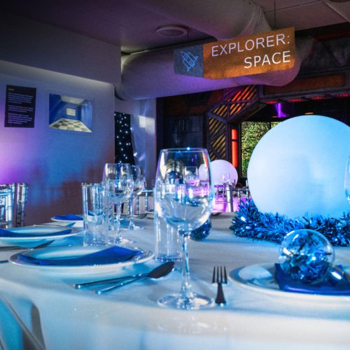 A dinner table with white tablecloth set up for Christmas dinner with space items in the background