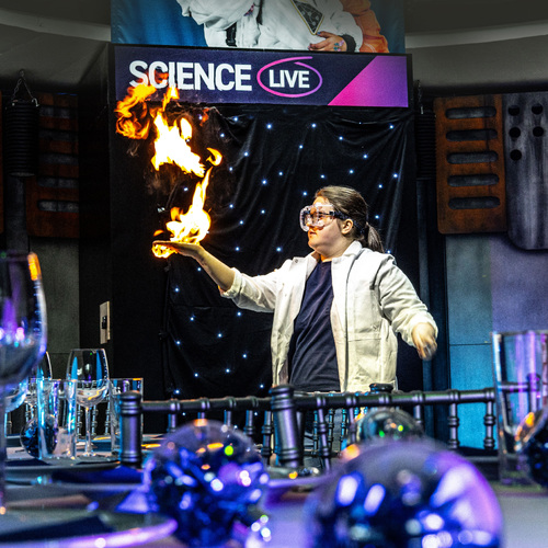 A scientist with her hand on fire behind a festive dinner table