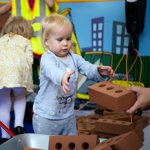 Interactive science exhibition photo showing a toddler reaching for a foam brick
