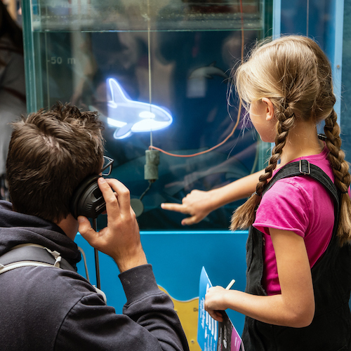 Interactive science exhibition photo showing a father and daughter looking and pointing at an exhibit