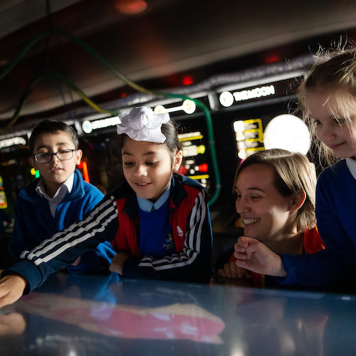 Interactive science exhibition photo showing a group of school children and a teacher looking and pointing at an exhibit about space