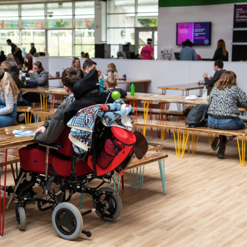A boy in a wheelchair sitting at one of the tables in The Hub Café upstairs