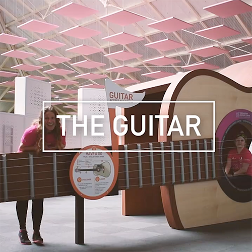 Interactive science exhibition photo showing a presenter leaning on the giant guitar