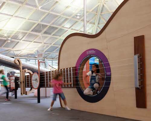 Interactive science exhibition photo showing two girls playing with a giant guitar