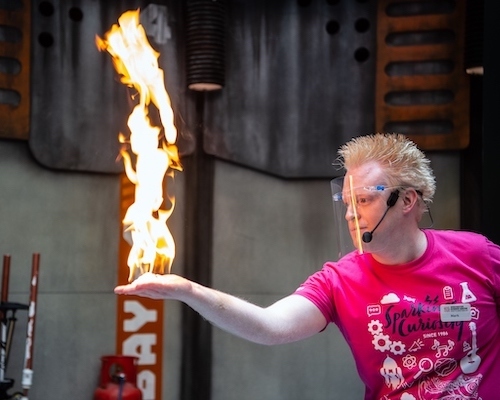 Live science demo area photo showing a presenter looking at his outstretched hand which appears to be on fire