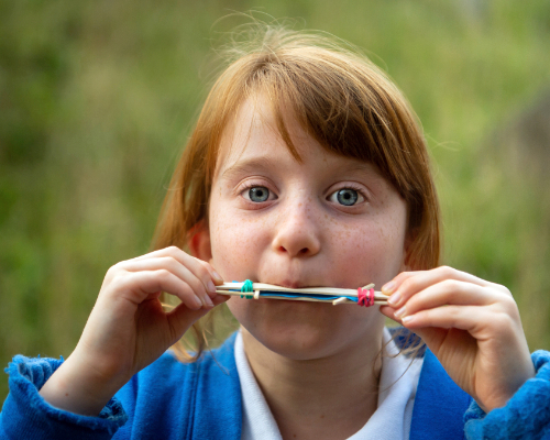 A young girl testing out a harmonica she has made