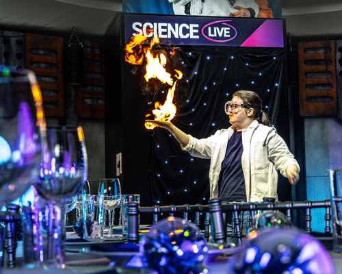 A scientist with her hand on fire behind a festive dinner table
