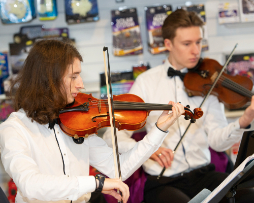 Two young smartly dressed males each playing the violin
