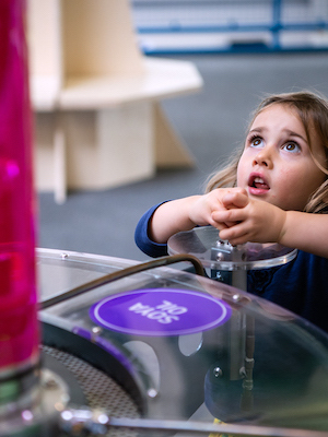 Interactive science exhibition photo showing a girl looking up in awe at some bubbles rising in a tube