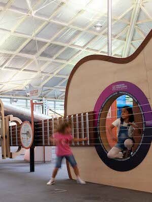 Interactive science exhibition photo showing two girls playing with a giant guitar