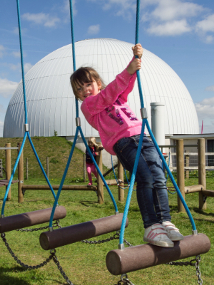 A young girl playing in the adventure playground with the Planetarium in the background