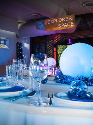 A dinner table with white tablecloth set up for Christmas dinner with space items in the background