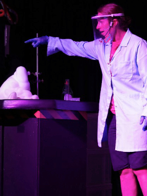 Live science show photo showing a female presenter in a lab coat pointing at a chemical reaction