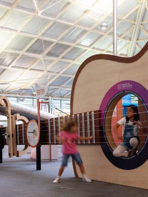 Interactive science exhibition photo showing two girls playing with a giant guitar