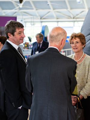 Two men, one with their back to us, interacting with a lady on the exhibition floor