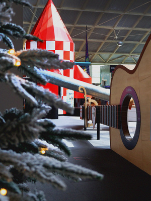 A snowy Christmas tree with a giant guitar and red and white rocket behind it